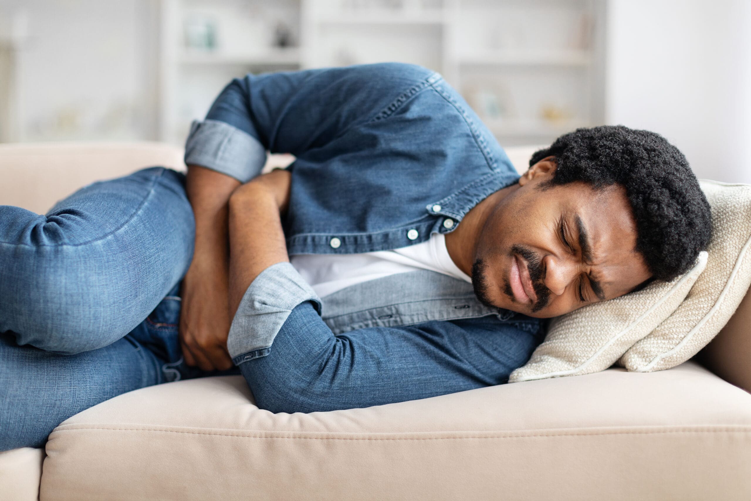 black-man-experiencing-stomach-pain-while-lying-couch-home-scaled.jpg