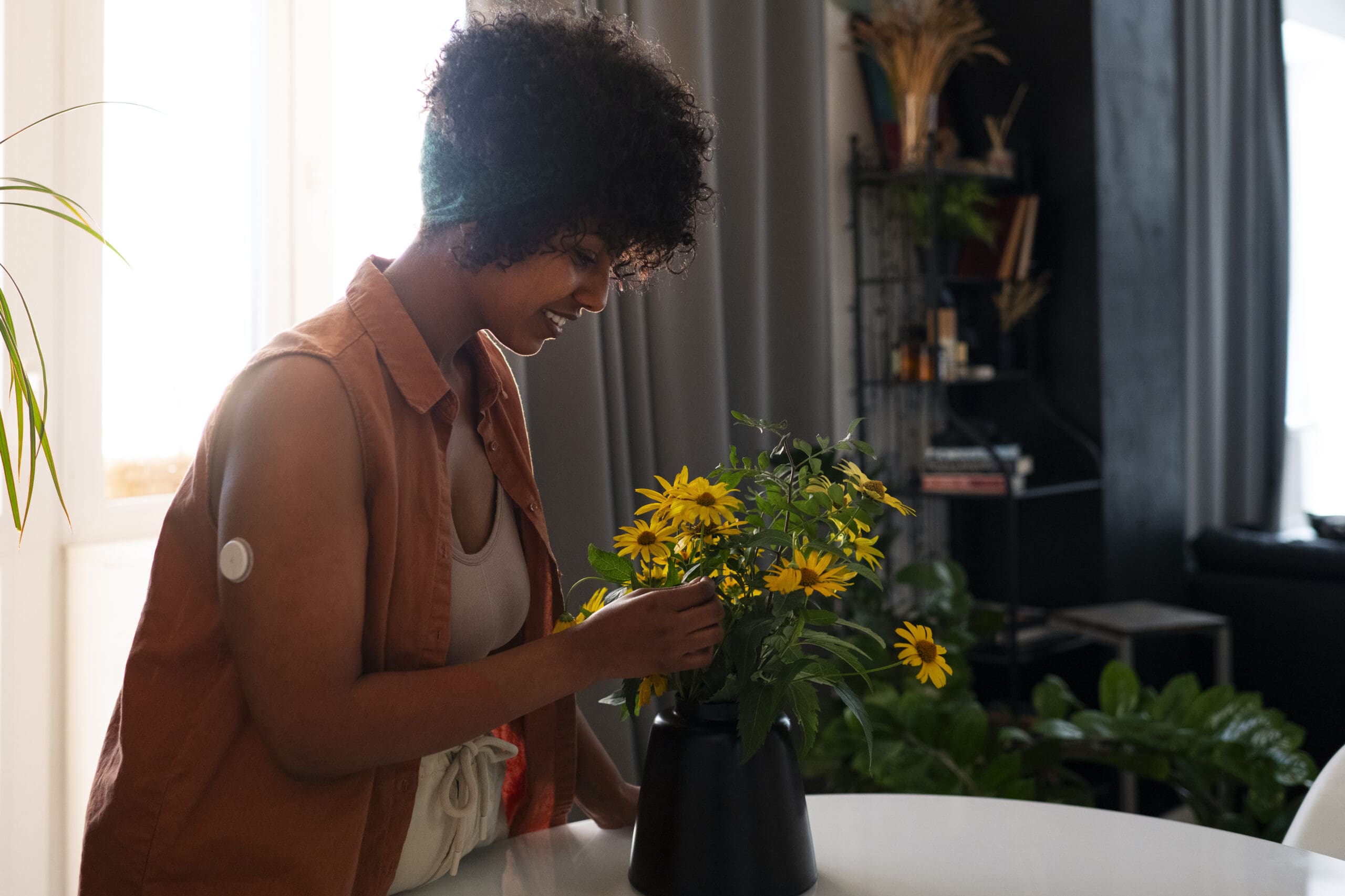 woman-wearing-glucose-patch-sensor-while-watering-plants-scaled.jpg