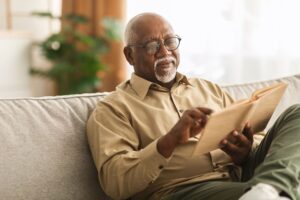 senior-african-american-man-reading-book-sitting-couch-home-scaled.jpg